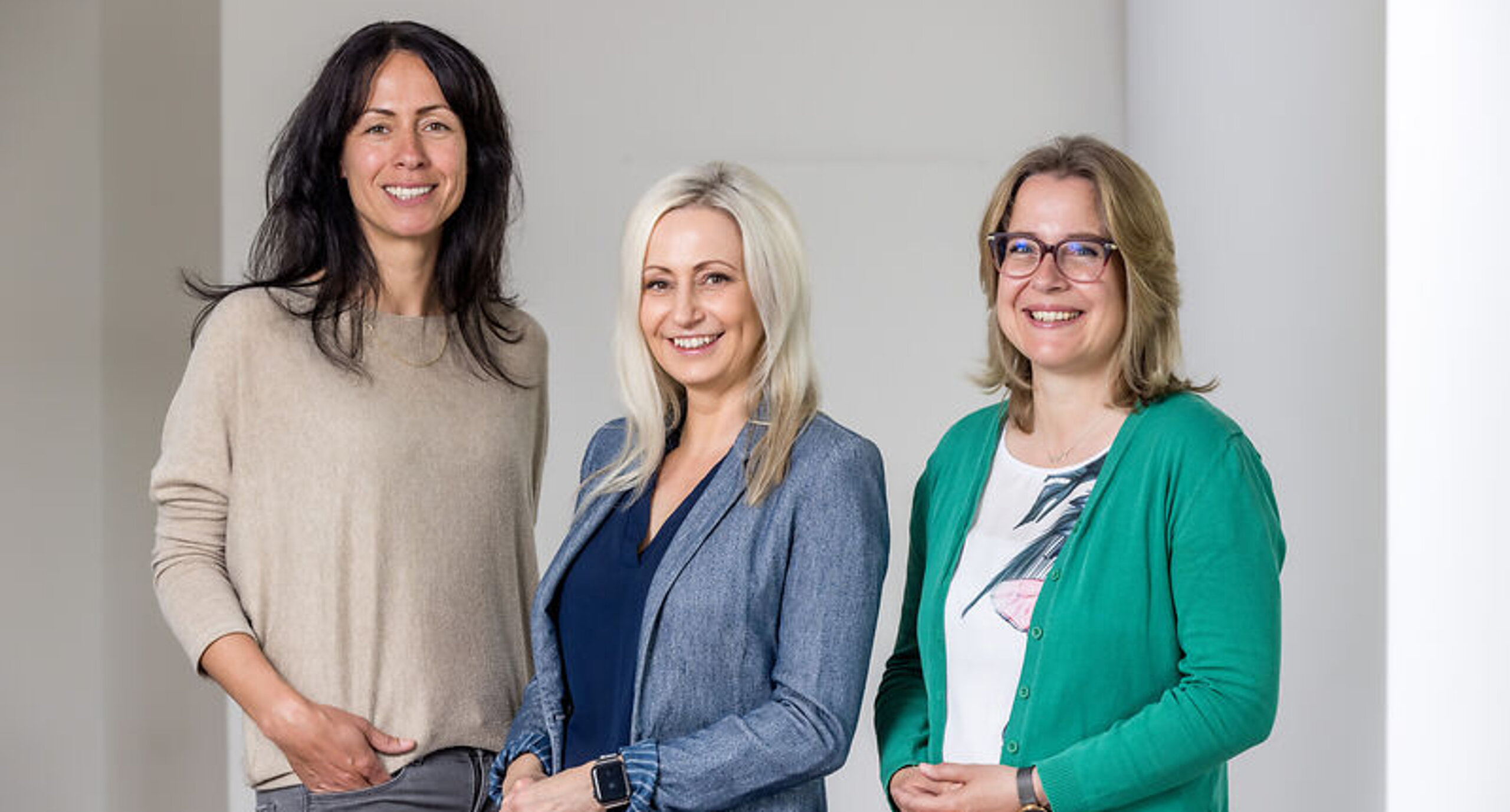 Das Bild zeigt drei Frauen, die in die Kamera lächeln.