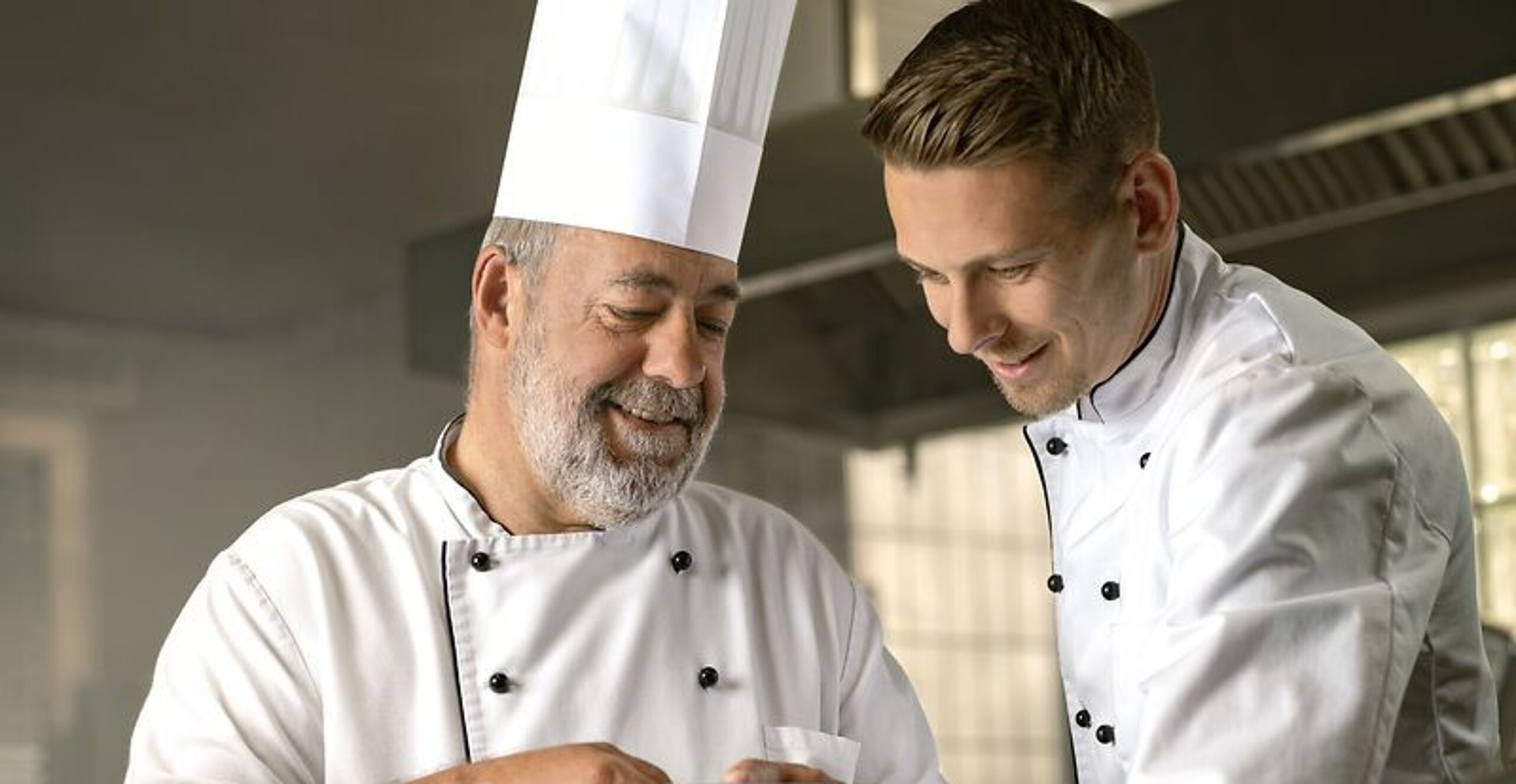 Ein alter Koch zeigt einem jungen Koch etwas.