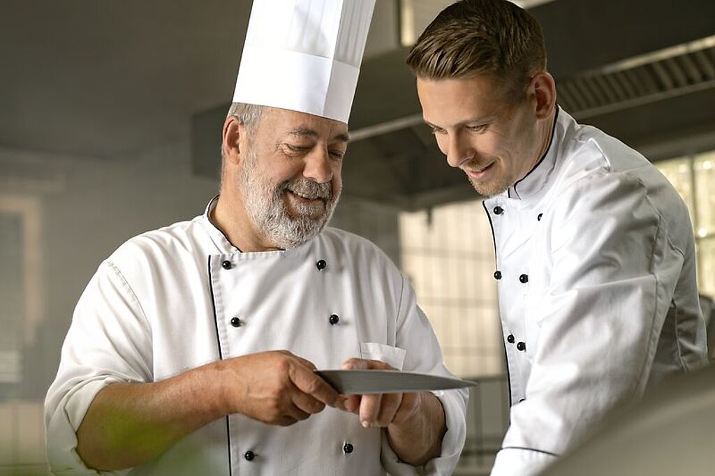 Respekt Ein alter Koch zeigt einem jungen Koch etwas.