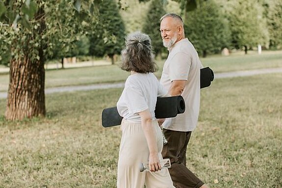 Patienten Outdoor Gymnastik Ein Mann und eine Frau laufen mit Gymnastikmatten auf einer Wiese.