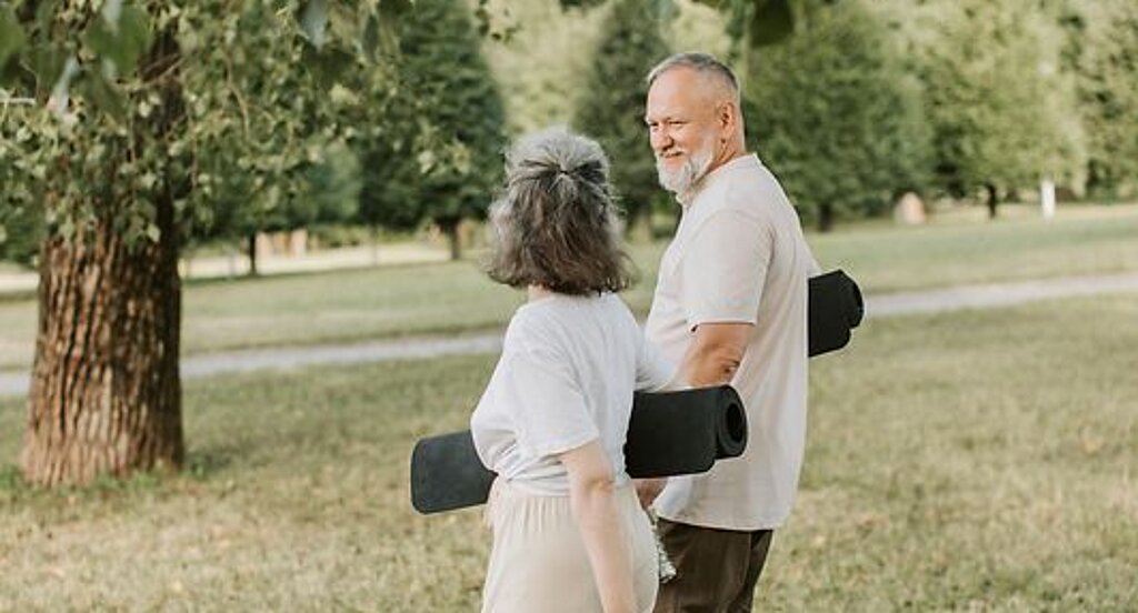 Patienten Outdoor Gymnastik Ein Mann und eine Frau laufen mit Gymnastikmatten auf einer Wiese.