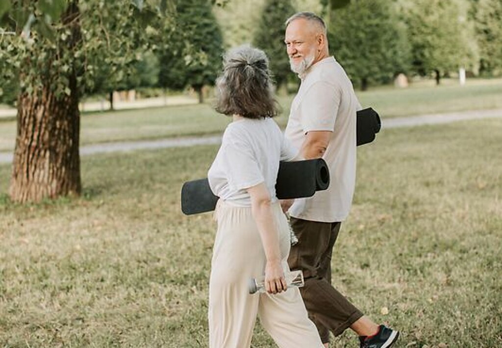 Patienten Outdoor Gymnastik Ein Mann und eine Frau laufen mit Gymnastikmatten auf einer Wiese.