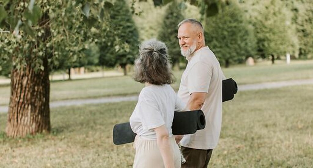 Patienten Outdoor Gymnastik Ein Mann und eine Frau laufen mit Gymnastikmatten auf einer Wiese.