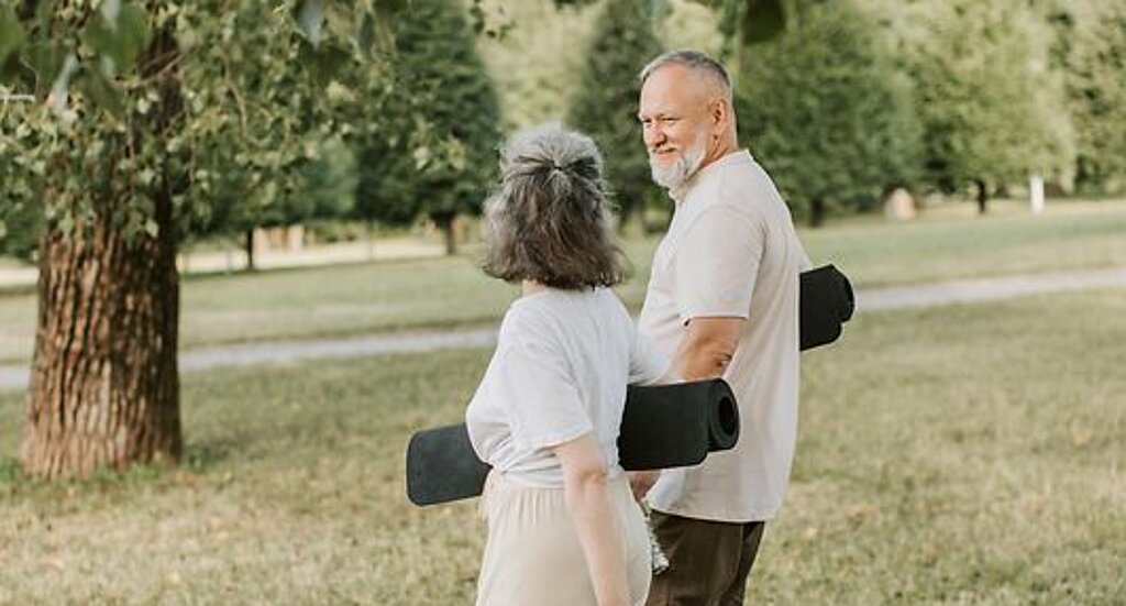 Patienten Outdoor Gymnastik Ein Mann und eine Frau laufen mit Gymnastikmatten auf einer Wiese.