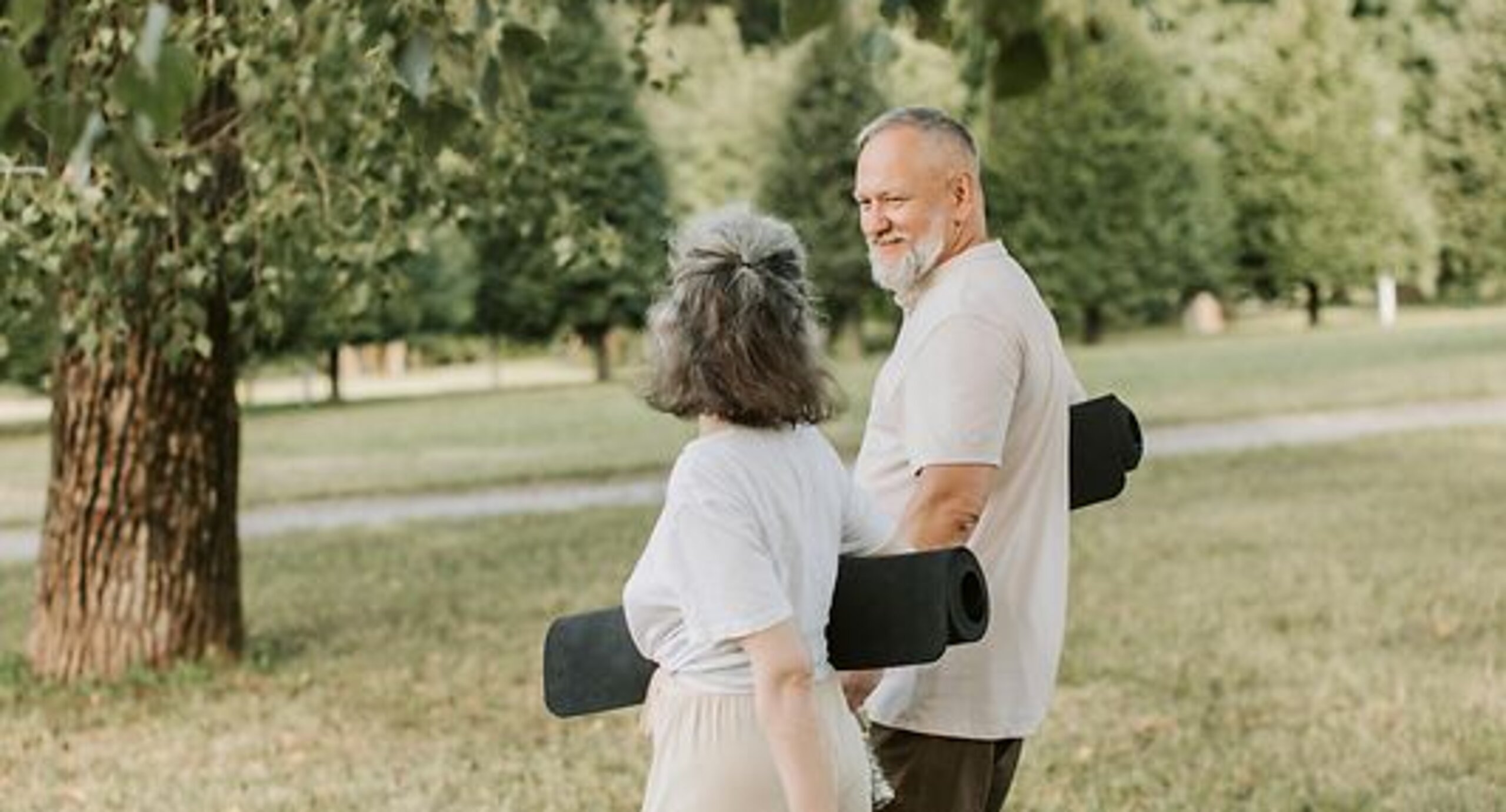 Patienten Outdoor Gymnastik Ein Mann und eine Frau laufen mit Gymnastikmatten auf einer Wiese.