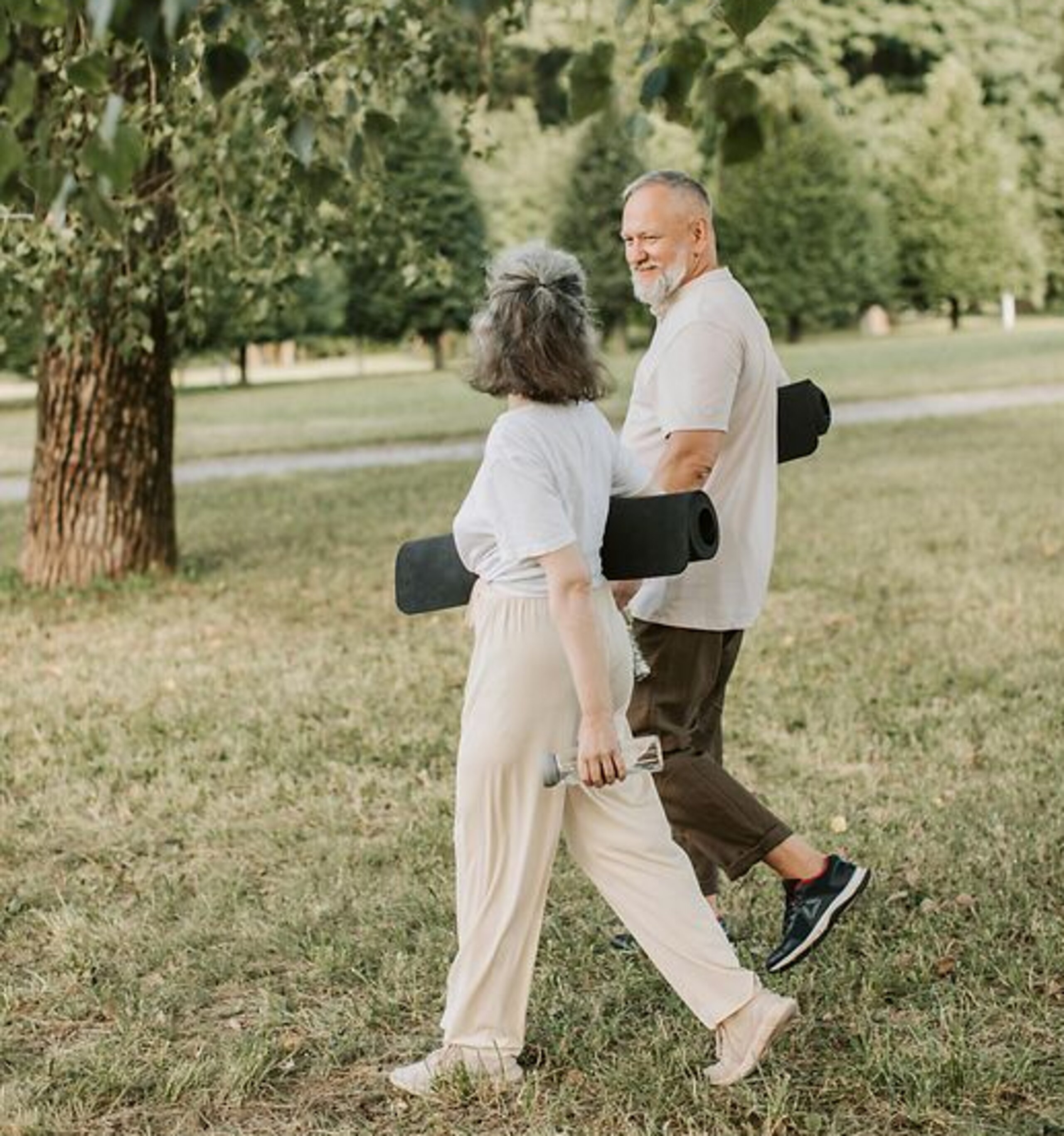 Patienten Outdoor Gymnastik Ein Mann und eine Frau laufen mit Gymnastikmatten auf einer Wiese.