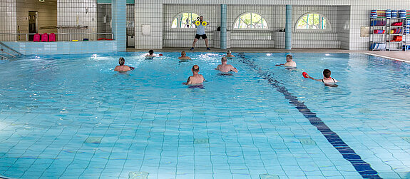 Ein Therapeut leitet eine Wassergymnastik-Gruppe an.