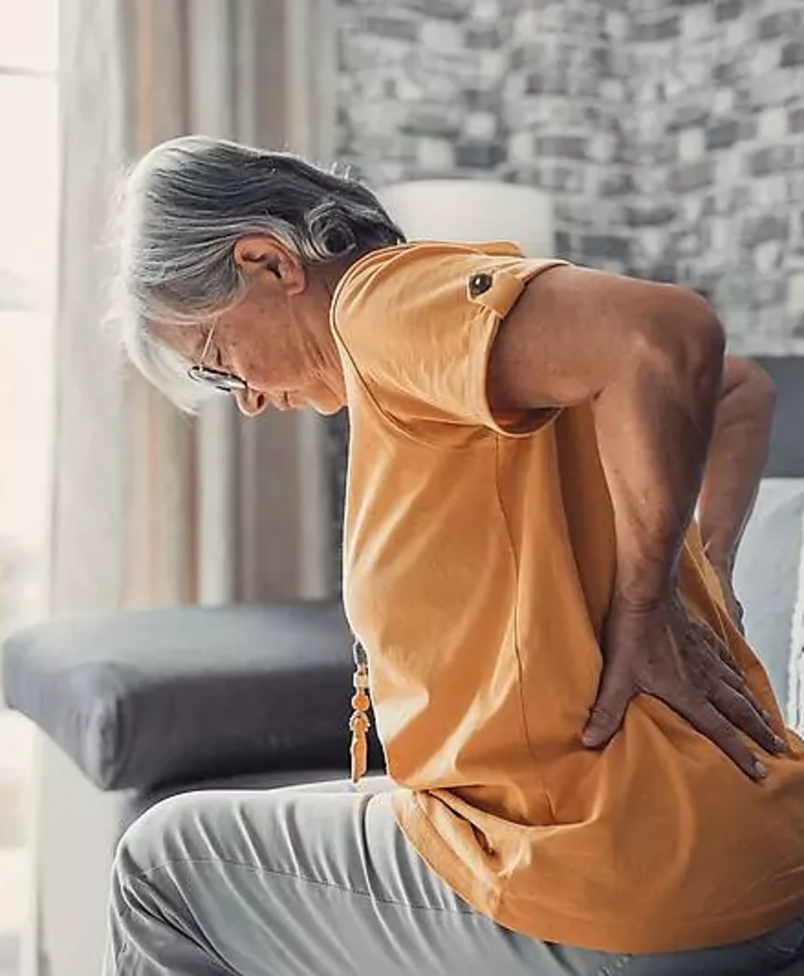 Eine Frau stützt die Hände schmerzhaft in die Lendenwirbelsäule.