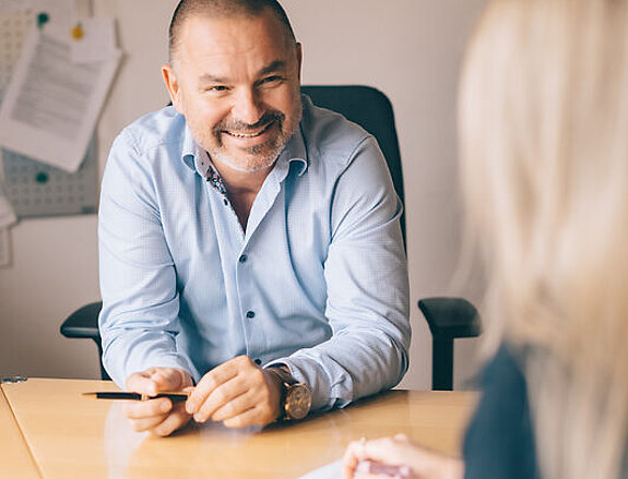 Maximilian Koehler Dr. Köhler sitzt lächeln am Schreibtisch mit einer Patientin.