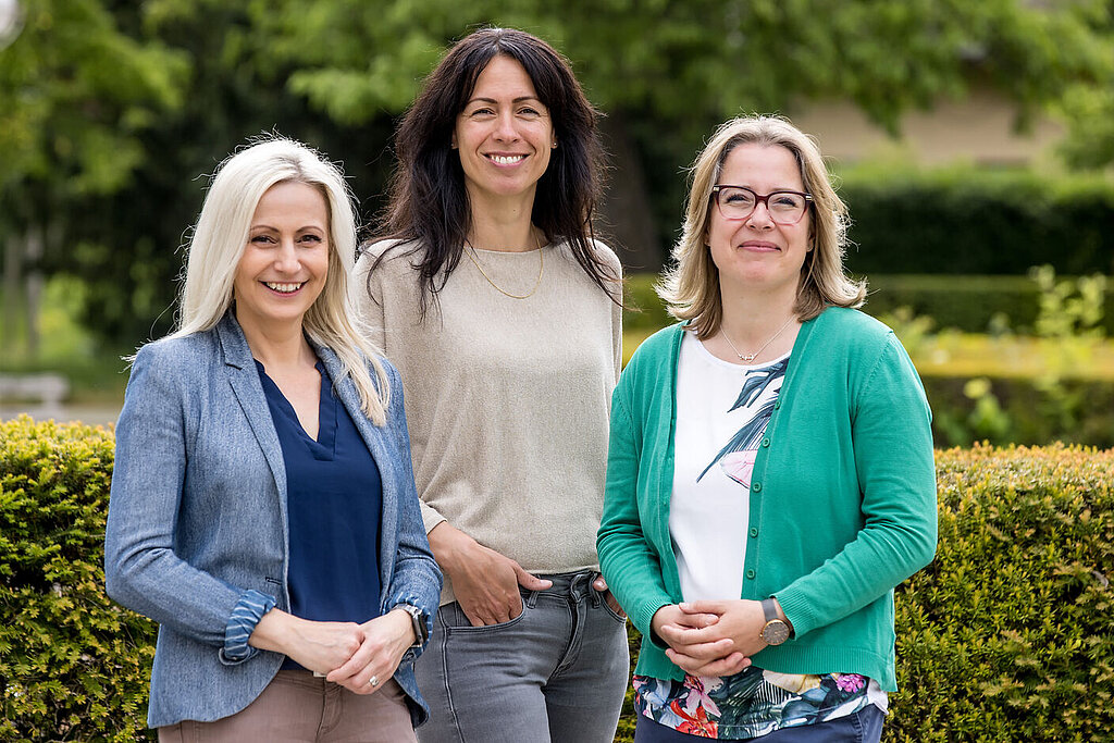 Sozialdienst Rehaklinik Bad Salzelmen Die drei Mitarbeiterinnen des Sozialdienstes sind zu einem Gruppenfoto im Kurpark aufgestellt und lächeln in die Kamera.