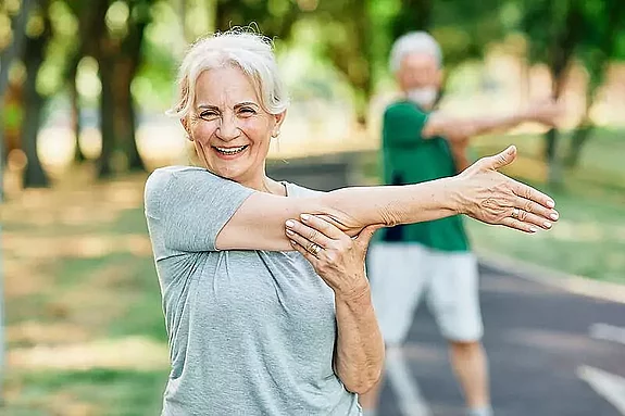 Gymnastik im Park Eine freundlich lächelnde Frau macht Dehnungsübungen im Park.
