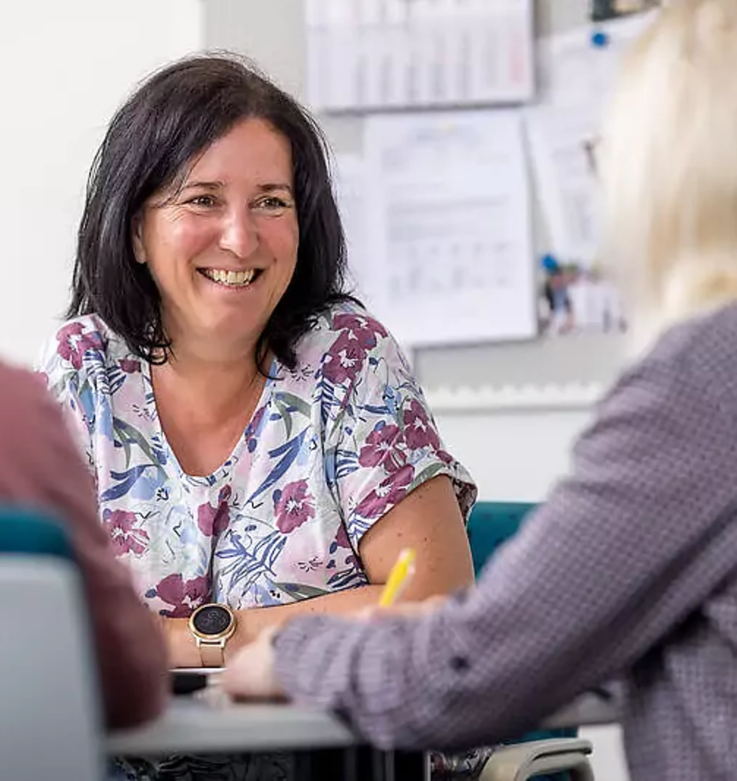 Eine Mitarbeiterin unterhält sich mit zwei Patienten am Schreibtisch.