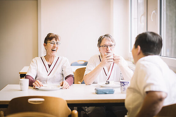 Drei Küchenhilfen sitzen gemeinsam am Tisch und lachen.