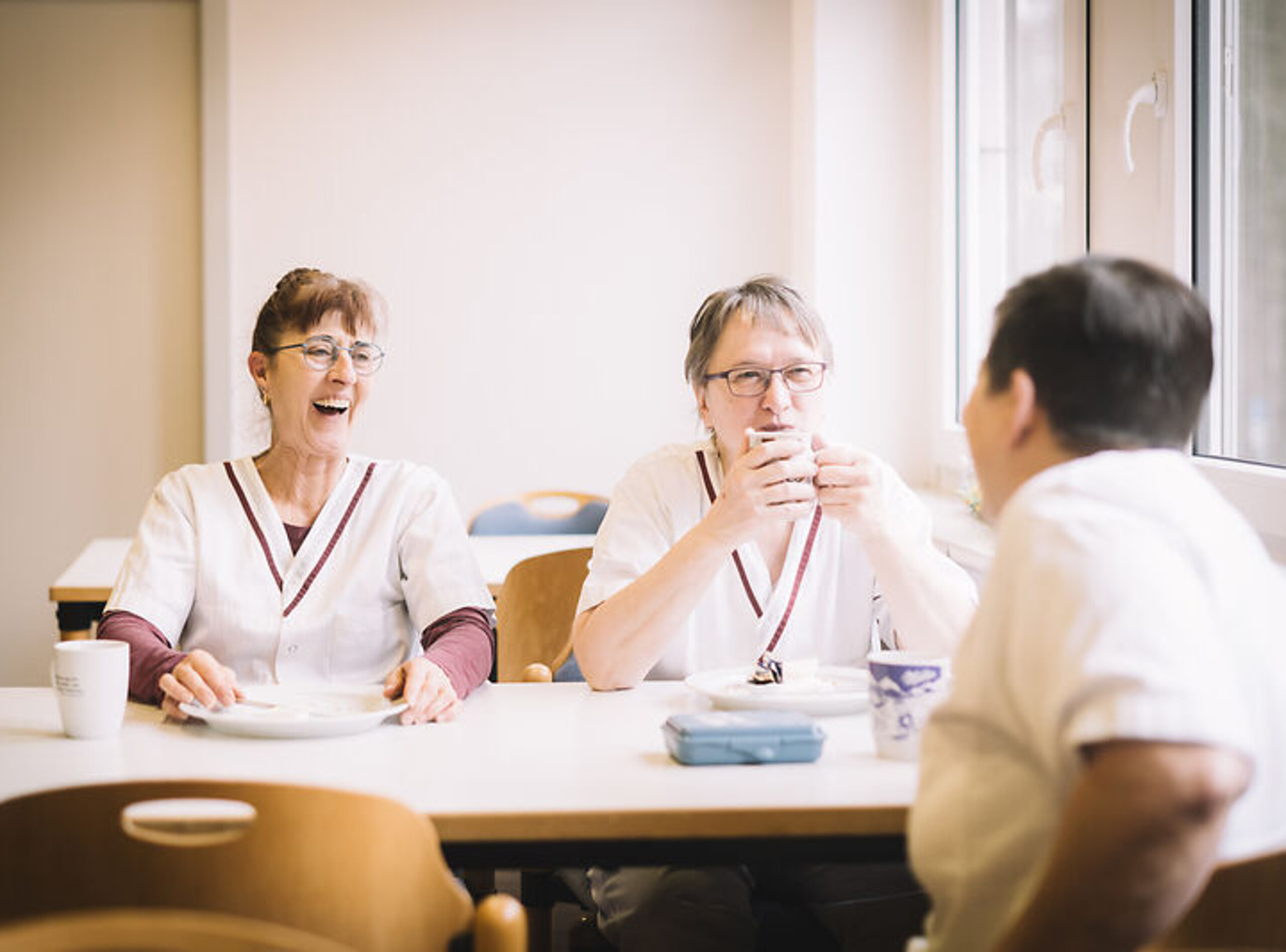 Drei Küchenhilfen sitzen gemeinsam am Tisch und lachen.