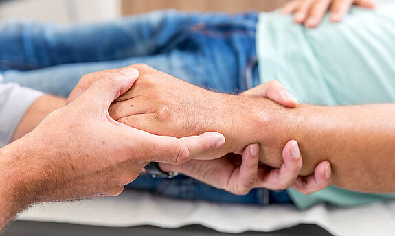 Ein Arzt umfasst die Hand eines Patienten.