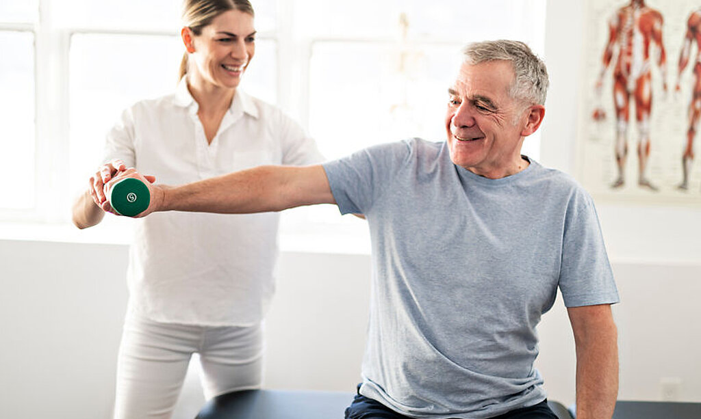 Eine Therapeutin macht Hantelübungen mit einem Patienten.