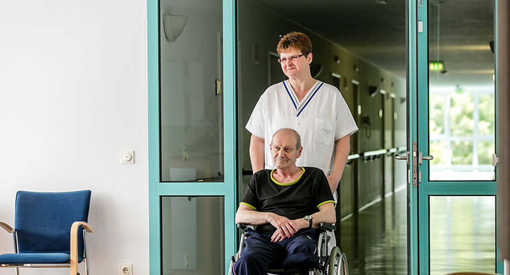 Eine Pflegekraft schiebt einen Rollstuhlpatienten
