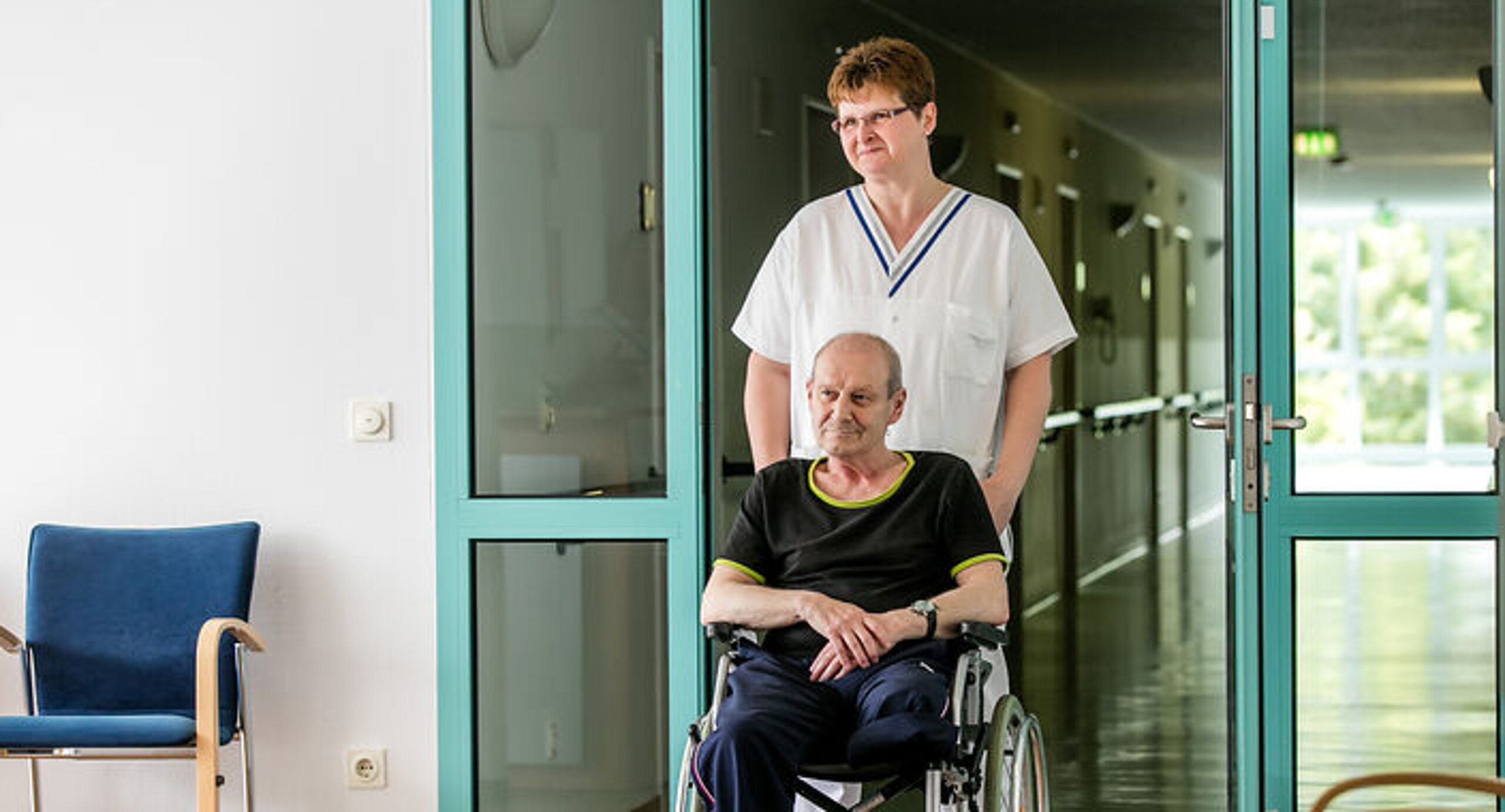 Eine Pflegekraft schiebt einen Rollstuhlpatienten
