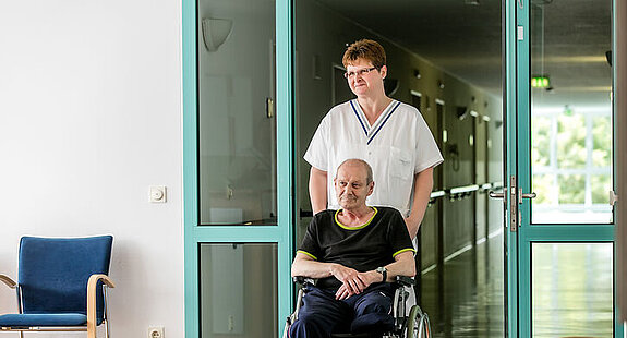Eine Pflegekraft schiebt einen Rollstuhlpatienten