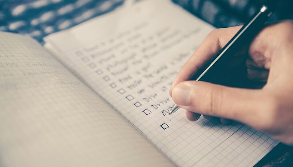 Jemand schreibt eine Checkliste in ein Notizbuch.