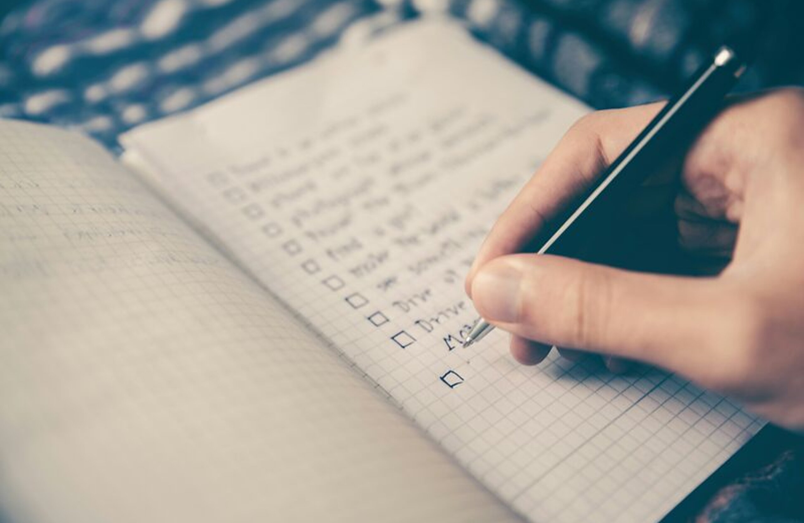 Jemand schreibt eine Checkliste in ein Notizbuch.