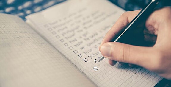 Jemand schreibt eine Checkliste in ein Notizbuch.