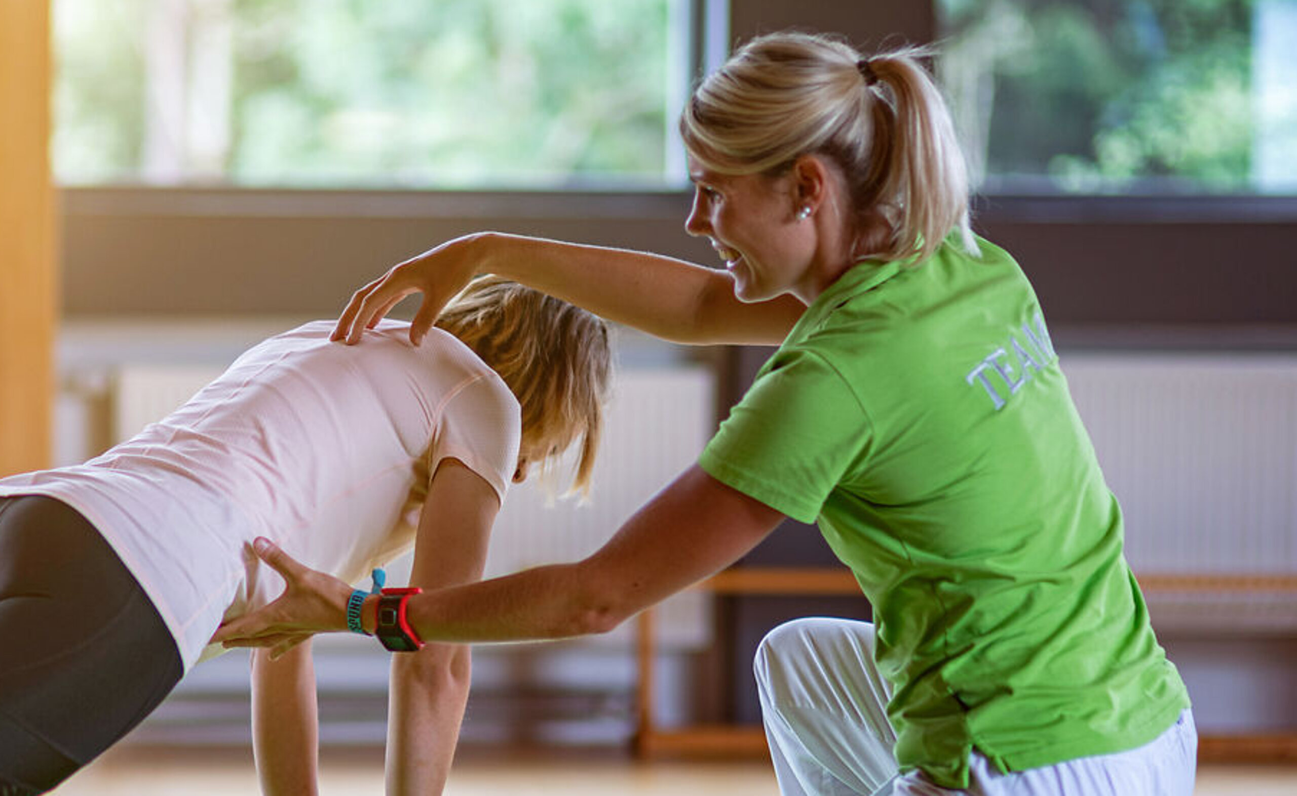 Eine Physiotherapeutin unterstützt eine junge Patientin bei einer Stützübung auf einem Ball.