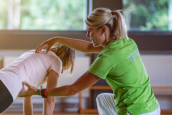 Physiotherapie mit Ball Eine Physiotherapeutin unterstützt eine junge Patientin bei einer Stützübung auf einem Ball.