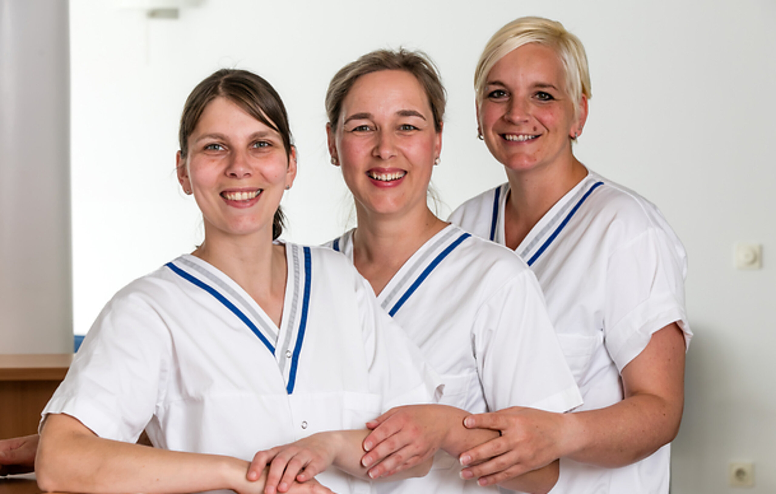 Pflegeteam Drei Pflegerinnen lächeln in die Kamera.