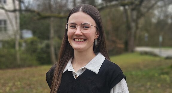 Eine junge Psychologin der KIH steht im Freien vor Bäumen und lächelt freundlich.