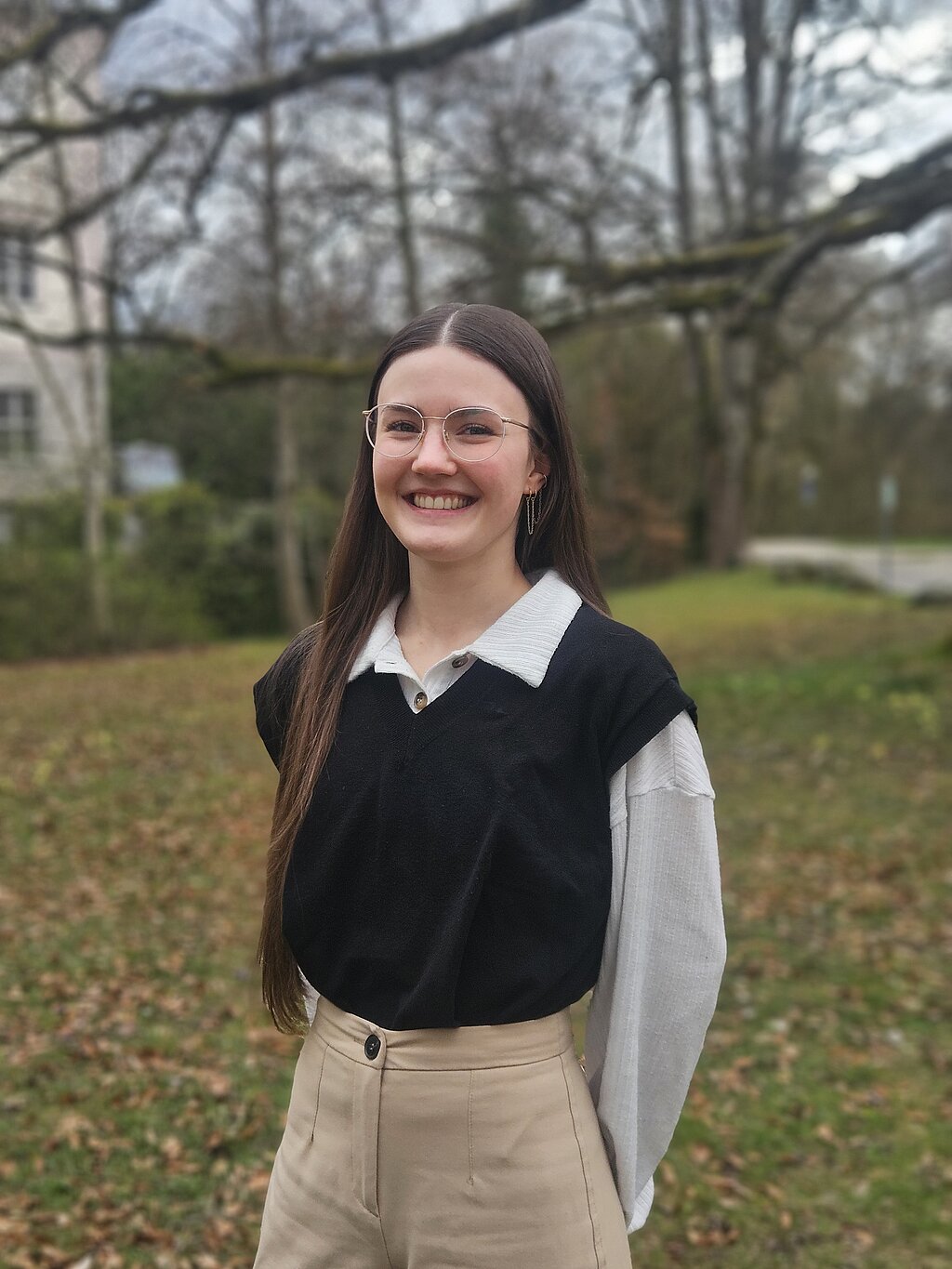 Eine junge Psychologin der KIH steht im Freien vor Bäumen und lächelt freundlich.