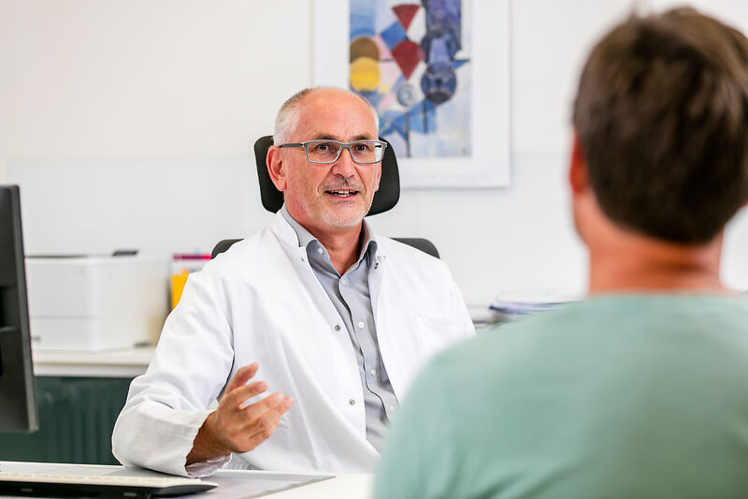 Artgespräch mit Patient Ein Arzt unterhält sich freundlich mit einem Pateinten am Schreibtisch.