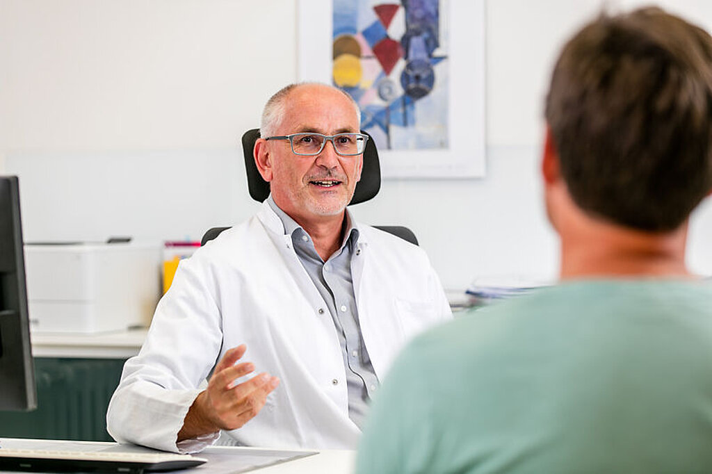 Artgespräch mit Patient Ein Arzt unterhält sich freundlich mit einem Pateinten am Schreibtisch.