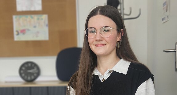 Eine Psychologin der KIH sitzt am Schreibtisch und guckt Richtung Kamera während sie einen Kugelschreiber hält.