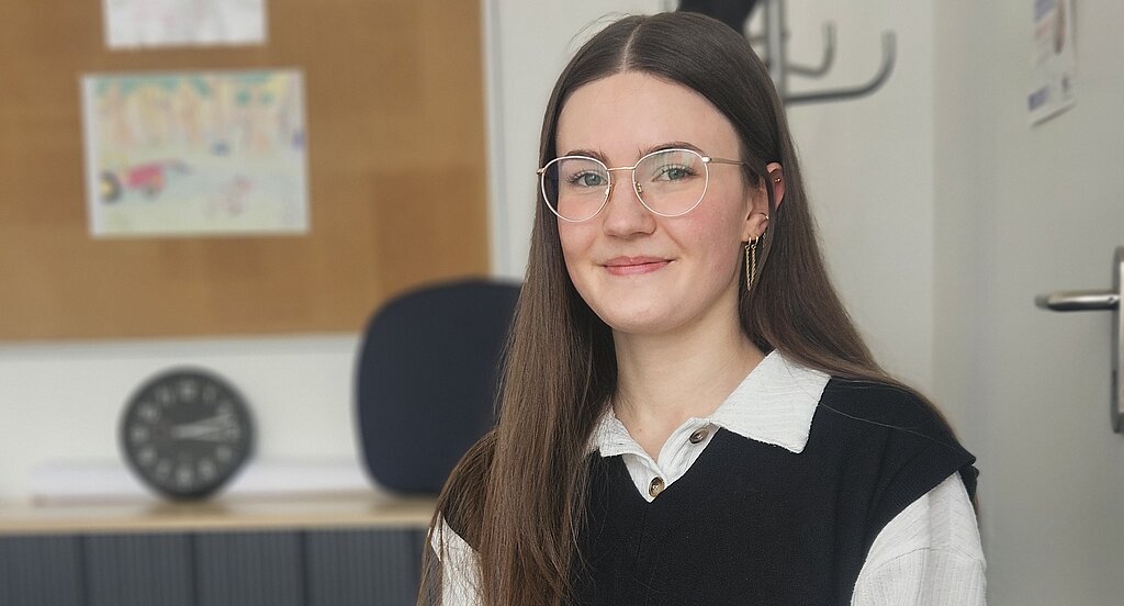 Eine Psychologin der KIH sitzt am Schreibtisch und guckt Richtung Kamera während sie einen Kugelschreiber hält.