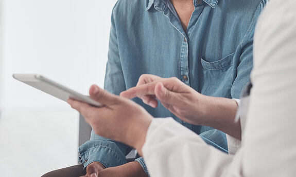 Eine Ärztin zeigt einer jungen Patientin etwas an einem Tablet.