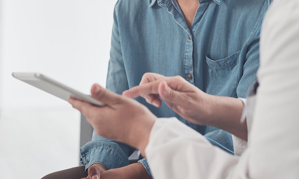 Eine Ärztin zeigt einer jungen Patientin etwas an einem Tablet.