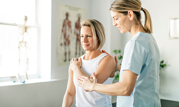 Eine Physiotherapeutin behandelt den Arm einer Patientin.