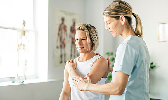 Eine Physiotherapeutin behandelt den Arm einer Patientin.