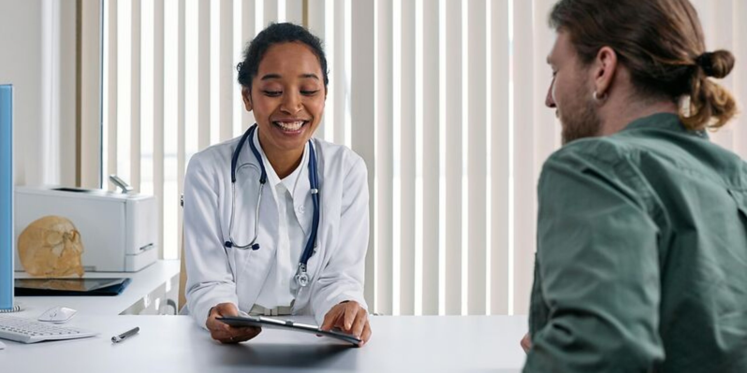 Eine Ärztin redet mit einem Patienten am Schreibtisch.