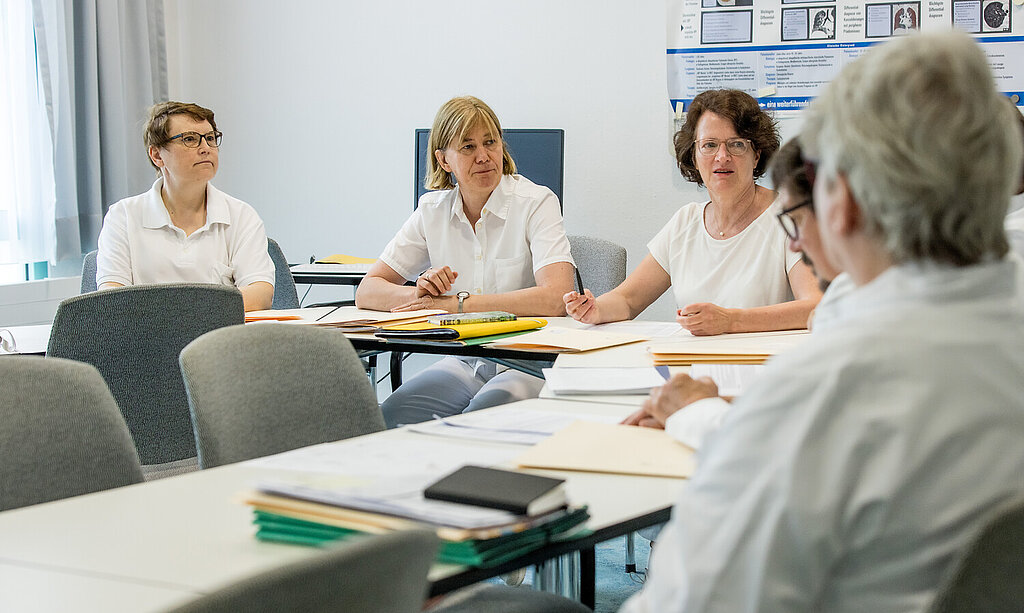 Eine Gruppe medizinische Angestellte sitzt gemeinsam am Tisch und spricht miteinander.