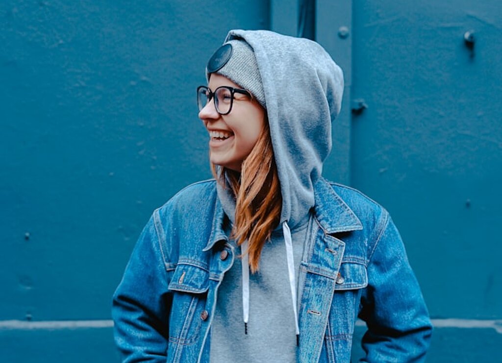 Eine Schülerin in Jeansjacke steht lachend vor einer blauen Wand.