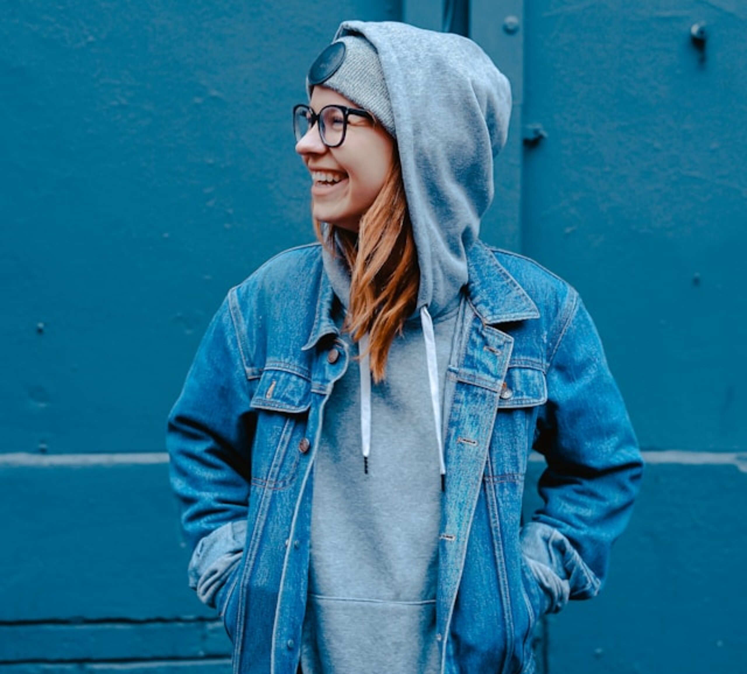 Eine Schülerin in Jeansjacke steht lachend vor einer blauen Wand.