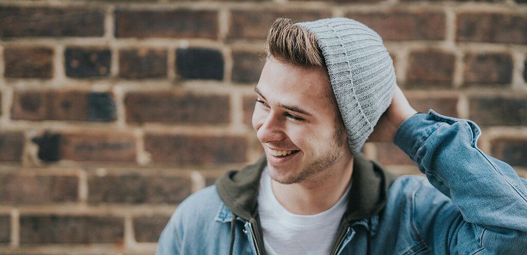 Ein lächelnder Jugendlicher mit Strickmütze vor einer Mauer.