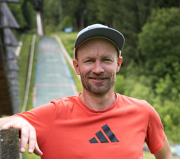 Maximilian Mechler steht vor einer Skisprungschanze.