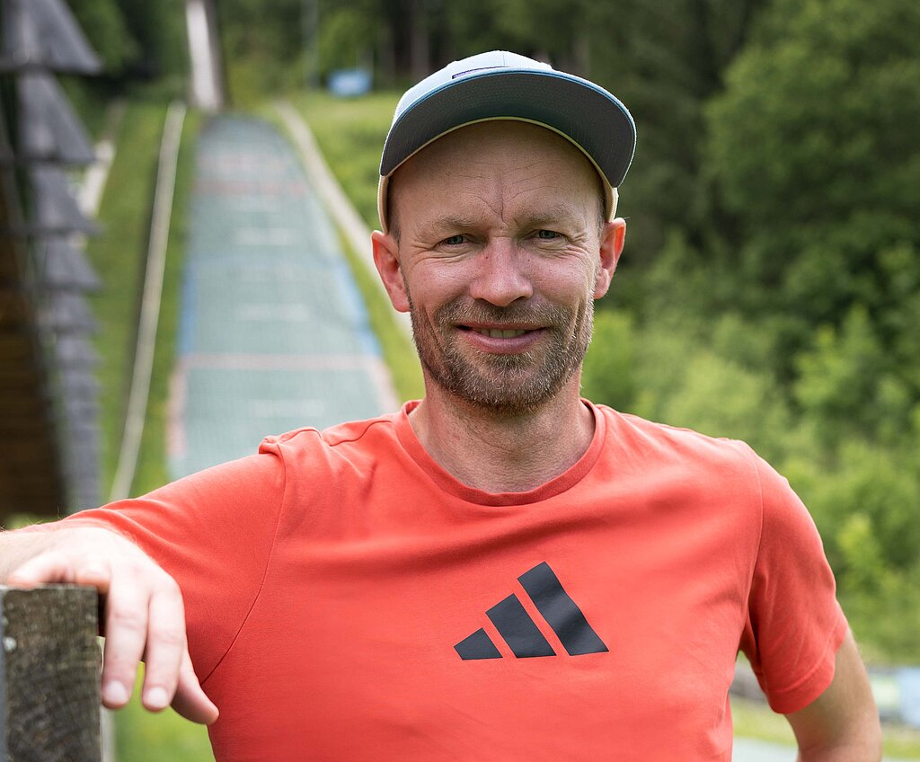 Maximilian Mechler steht vor einer Skisprungschanze.