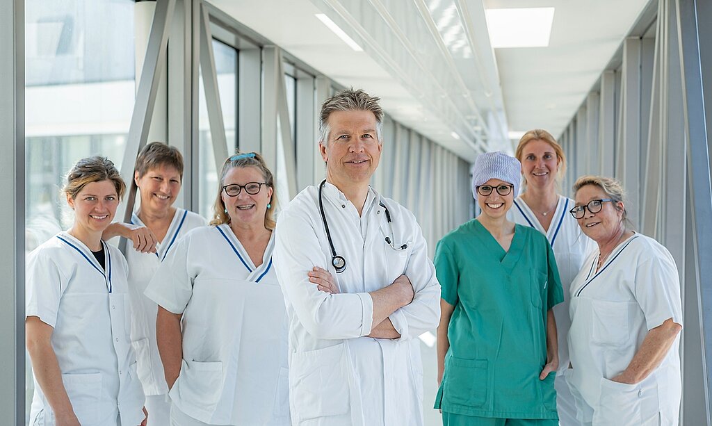 Ein Team aus Arzt und mehreren Pflegekräften steht in einem Glasgang.