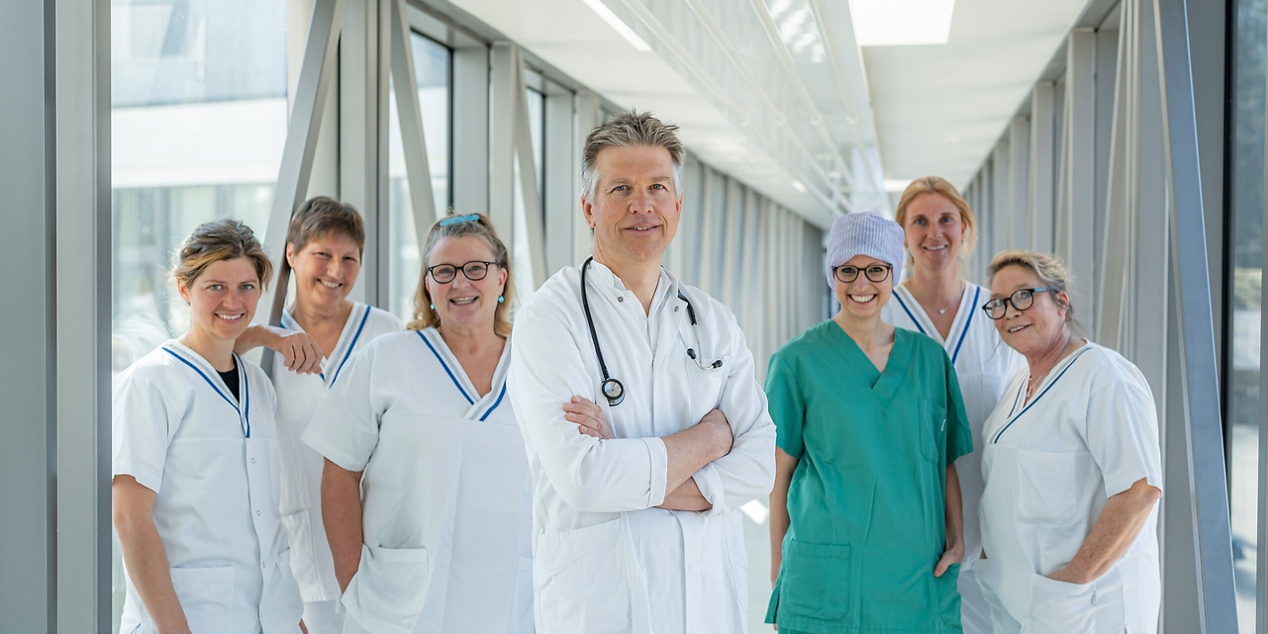 Ein Team aus Arzt und mehreren Pflegekräften steht in einem Glasgang.