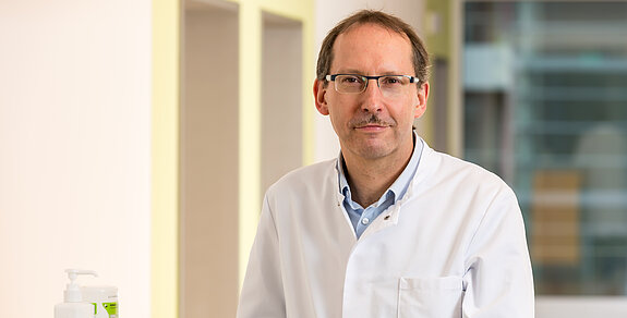 Dr. Klaus Müller, Chefarzt der Klinik im Hofgarten, steht an einem Stationswagen und lächelt freundlich