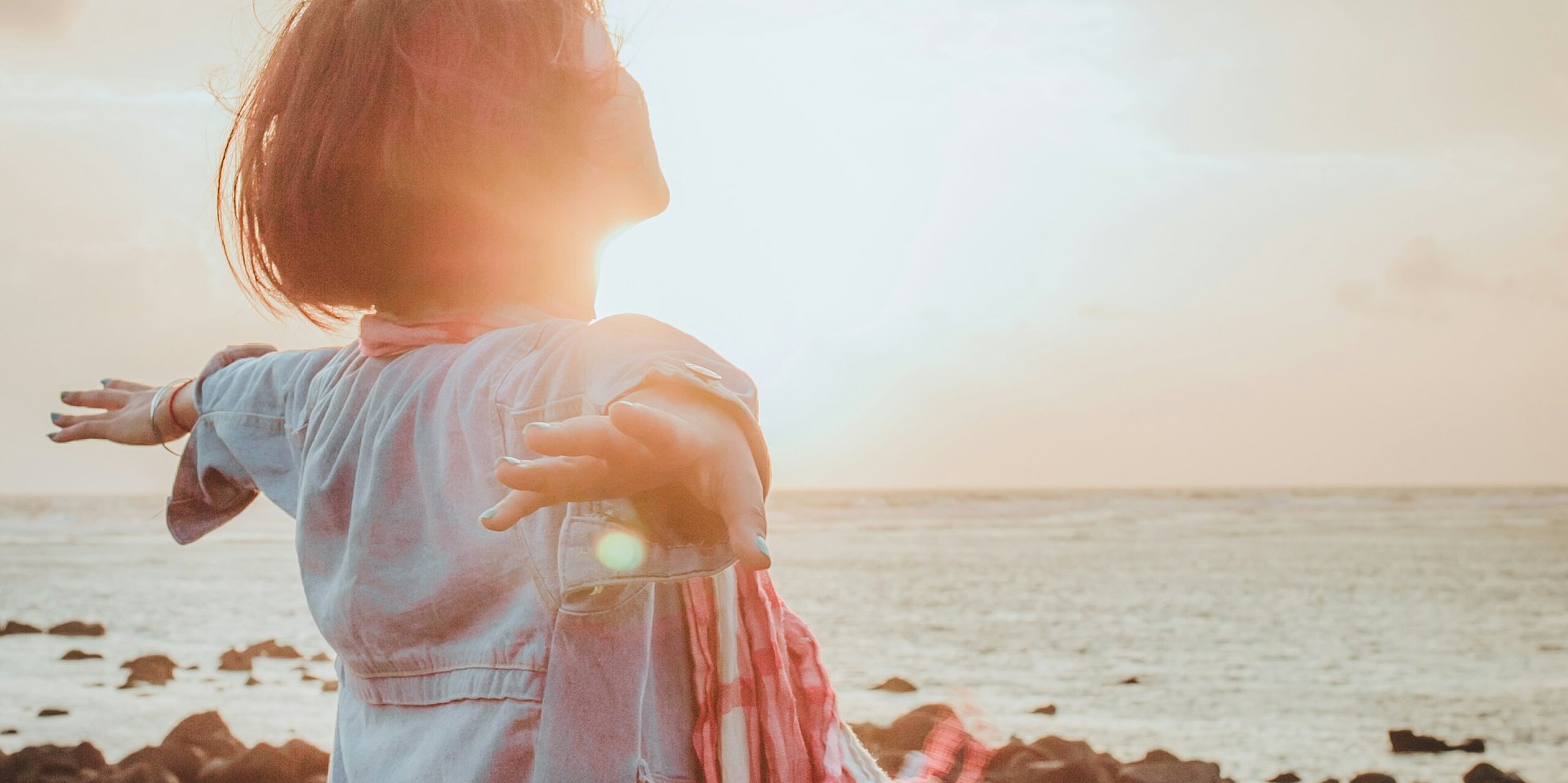 Eine Frau atmet tief ein mit ausgebreiteten Händen am Meer.